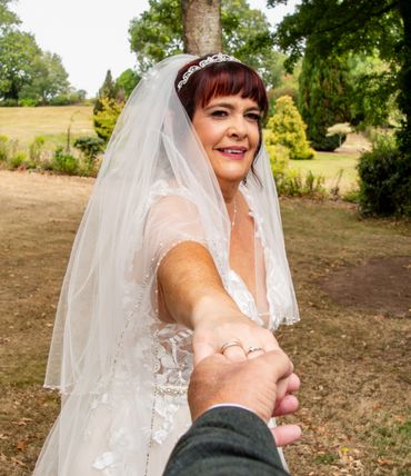 Bride smiling and holding hand outdoors in a wedding dress and veil.