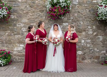 Bride in white gown with three bridesmaids in burgundy dresses holding bouquets.