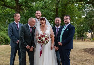 Bride smiling with groomsmen and family in a garden setting.