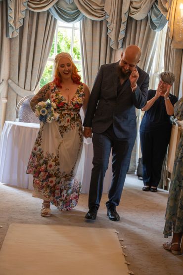 Happy couple holding hands and smiling, walking down an aisle indoors.