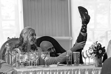 A joyful moment of a man lifting his leg while a woman laughs at a dining table.
