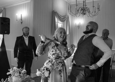 Woman playfully holding a knife behind a surprised man at a formal event.