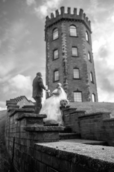 Black and white photo of a couple near a stone tower on a cloudy day.