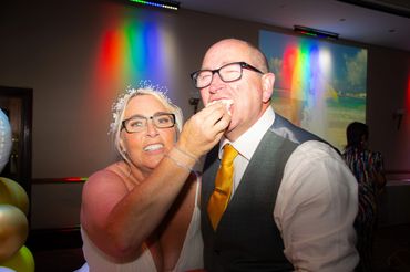 Bride feeding groom cake at wedding reception with colorful lights.