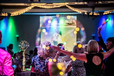 People dancing energetically at a colorful party with glowing lights and decorations.