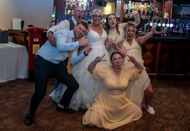 A lively group poses with fun hand gestures at a wedding reception.