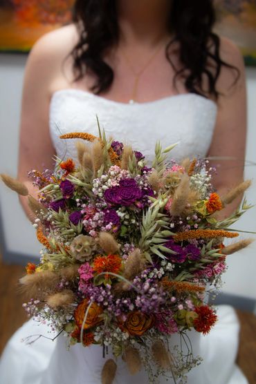 Bride in white dress holding a vibrant dried flower bouquet.
