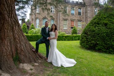 Newlyweds pose happily in front of a historic stone building on their wedding day.