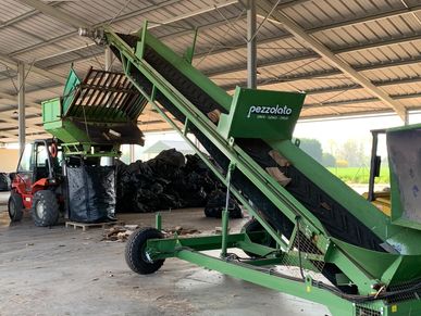 Green agricultural machinery with conveyor belts inside a warehouse.