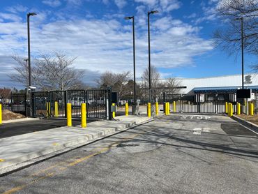 Secure gated entrance with yellow bollards and stop sign under a partly cloudy blue sky.