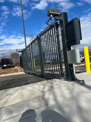 Automatic metal security gate at a parking lot entrance on a sunny day.