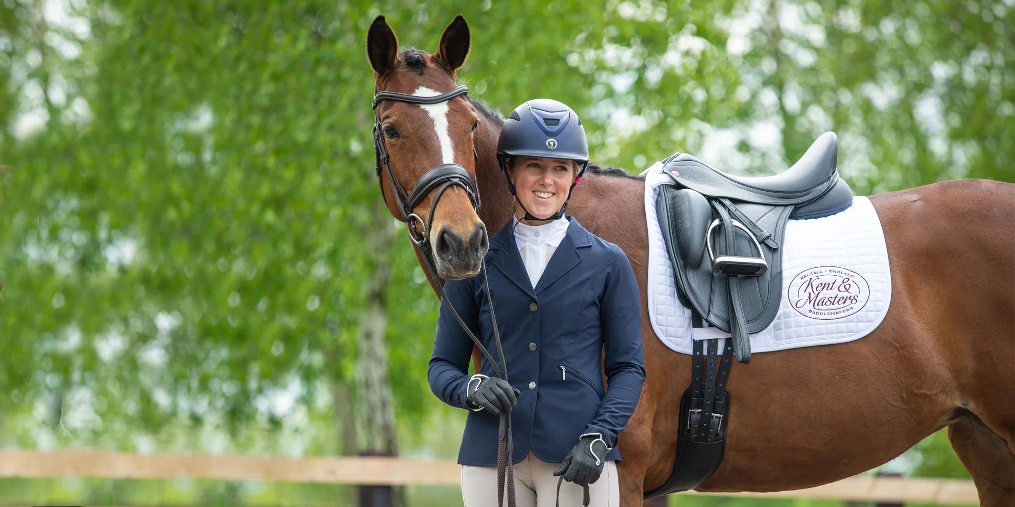 Female equestrian standing with a brown horse outdoors.