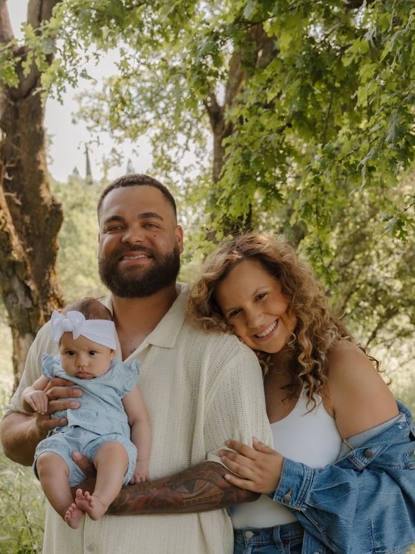 Happy family with a father holding a baby and mother hugging him outdoors.