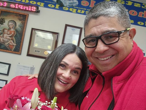 A smiling couple in red outfits holding a bouquet of flowers indoors.