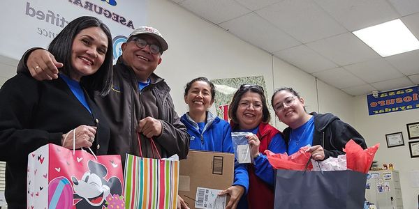 A group of five people smiling and holding gift bags and a box indoors.