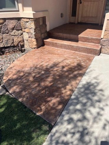 Stone-patterned concrete steps and patio leading to a wooden front door.
