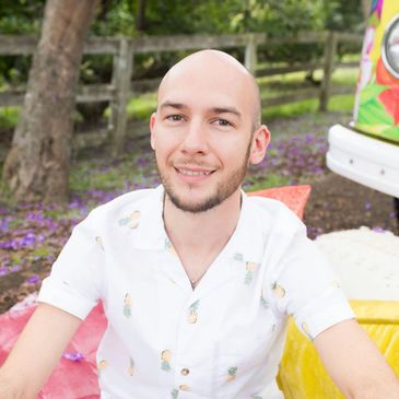 Smiling man in a pineapple-patterned shirt outdoors.
