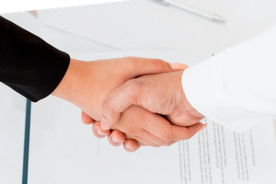 Two people shaking hands over a document in a professional setting.