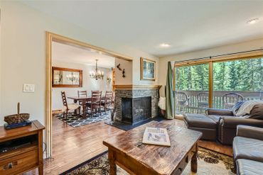 Cozy living room with stone fireplace and dining area, featuring wooden furniture and forest views.