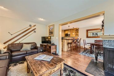 Cozy living room with leather sofas and rustic decor, opening to a kitchen and dining area.