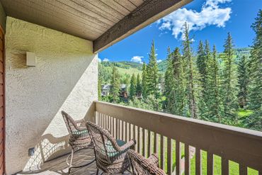 Balcony with wicker chairs overlooking a lush forest and mountains.