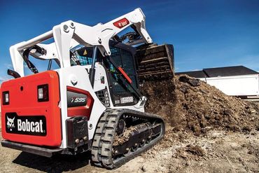 A white and red tractor is digging in the dirt.