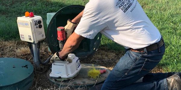 Jeremiah repairing an underground septic system in a grassy field.