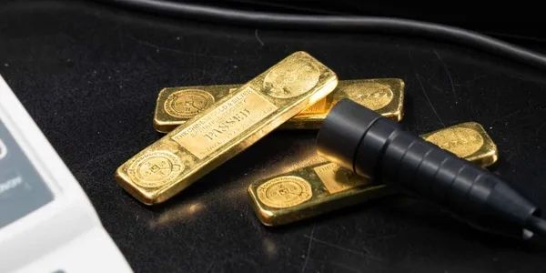 Gold bars and a black cable on a dark surface with a white device edge.