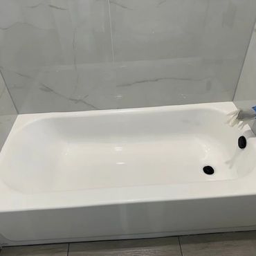 A clean white bathtub in a modern bathroom with marble walls.