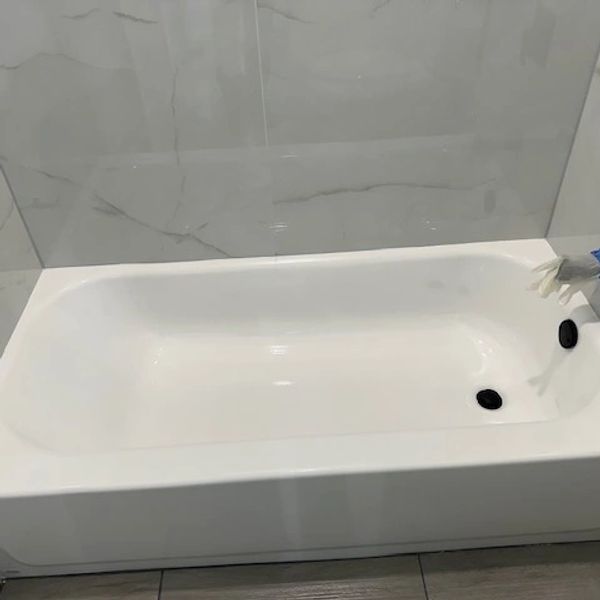 A clean white bathtub in a modern bathroom with marble walls.