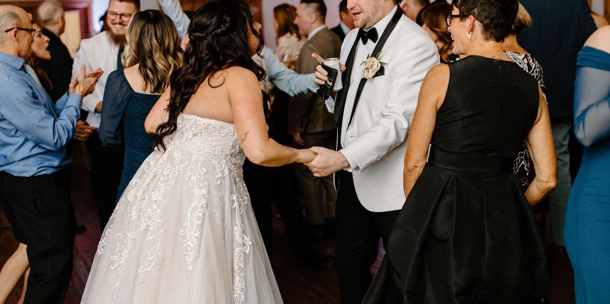 A bride and groom dance happily at their wedding reception surrounded by guests.