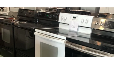 A row of various electric stoves in black, white, and stainless steel finishes.