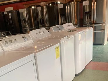 A row of white washing machines in a store with refrigerators in the background.