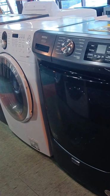 A black Maytag dryer next to a white washing machine on a tiled floor.