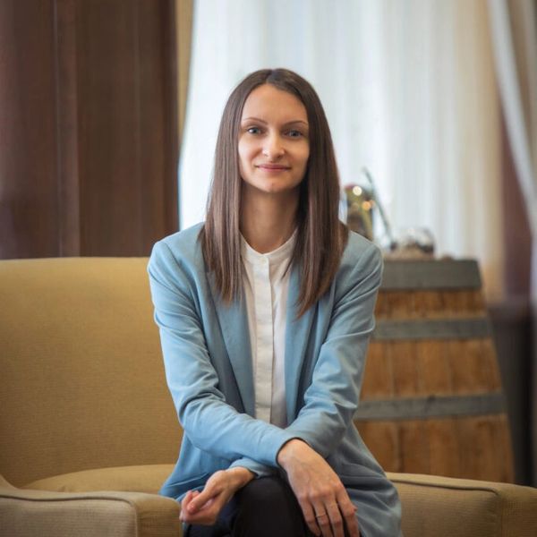 Professional woman sitting on a beige couch, wearing a light blue blazer and white shirt.