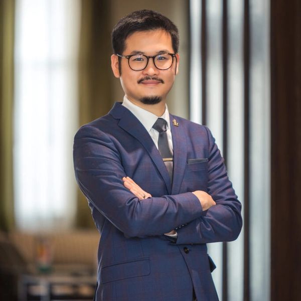 Confident man in a blue suit and glasses poses with arms crossed.