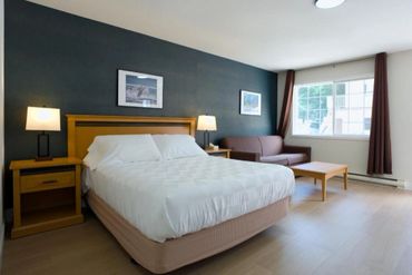 Bright hotel room with a cozy bed and sofa near a large window.