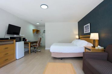 Simple and clean hotel room with bed, desk, TV, and cozy chair.