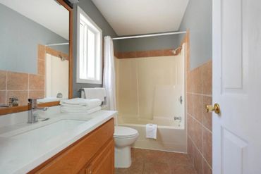 A clean bathroom with a bathtub, toilet, and wooden vanity with a large mirror.