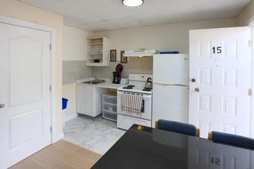 Small kitchenette with white appliances and an open door numbered 15.