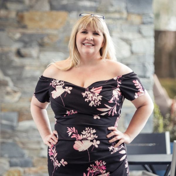 Smiling woman in a floral off-shoulder dress poses confidently outdoors.