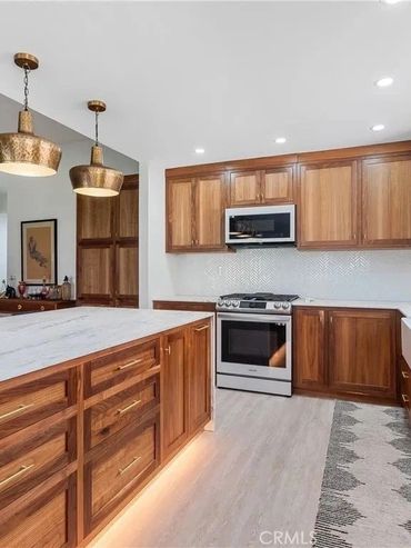 Modern kitchen with wooden cabinets, marble island, and brass pendant lights.