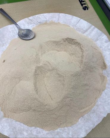 Fine beige powder spread on a white paper with a spoon beside it.