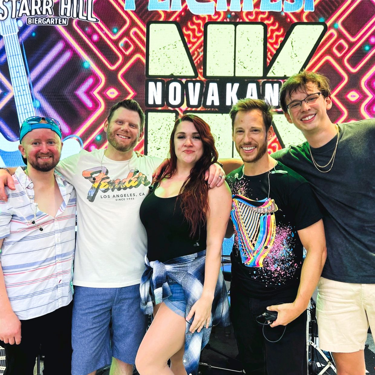 A happy group of five friends posing together at a music event.