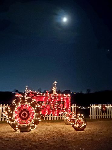 Red tractor decorated with string lights under a bright moonlit sky.