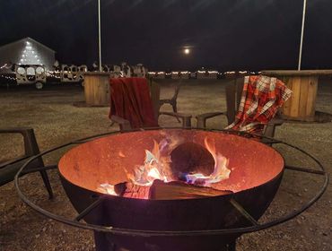 A cozy fire pit with red and plaid blankets on chairs at night.