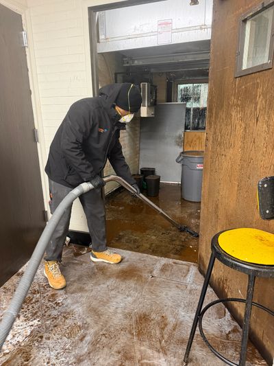 Person cleaning a dirty floor with a vacuum-like tool indoors.
