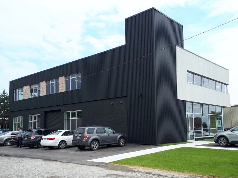 A modern commercial building with black metal siding and a white stucco mass above storefront glass.
