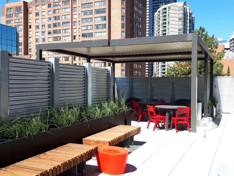 A grey metal pergola with a corrugated metal panel fence and paver stones on the building's rooftop.