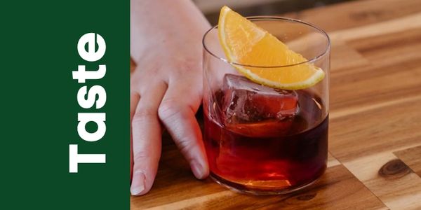 A hand holding a glass of red beverage with an orange slice.